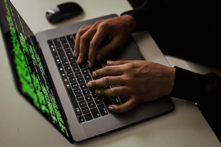 From above of crop anonymous male hacker typing on netbook with data on screen while sitting at desk